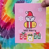 hand holding pink Bee Merry singing holiday card with bee wearing Santa hat, qr code that plays song