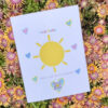 welcome new baby card with sun and hearts seen on bed of flowers