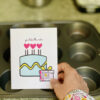 hand holding You Take the Cake singing birthday card in front of baking tin