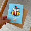hand holding holiday card with bee wearing Santa Hat and qr code that plays bees on earth song