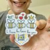 smiling woman holding diecut sticker with three smiling bees, icons and qr code that plays original song