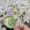 diecut sticker with duck and qr code that plays song held in front of bouquet of white flowers