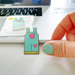 hand reaching for enamel pin with overalls