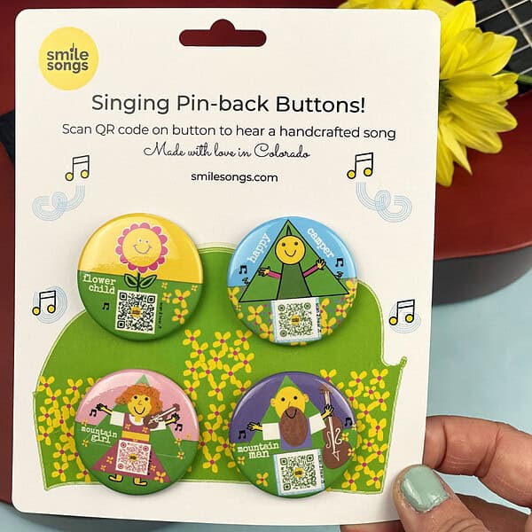 smile songs pinback buttons that sing photograph of pack of four pinback buttons with qr codes on art that sings and colorful characters. features pink mountain girl; purple mountain man, blue happy camper and yellow flower child pin