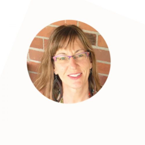 marj photo smiling woman with eyeglasses, shoulder length hair smiling at camera with brick wall behind her